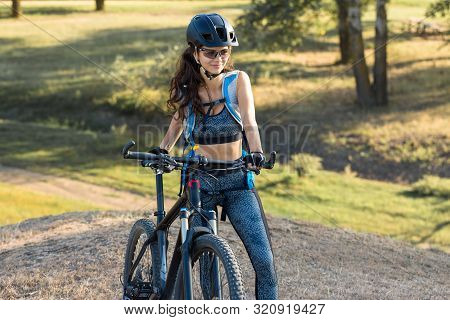 Girl On A Mountain Bike On Offroad, Beautiful Portrait Of A Cyclist At Sunset, Fitness Girl Rides A 