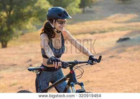 Girl On A Mountain Bike On Offroad, Beautiful Portrait Of A Cyclist At Sunset, Fitness Girl Rides A 