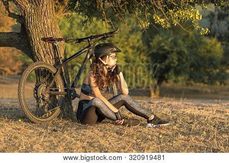 Girl On A Mountain Bike On Offroad, Beautiful Portrait Of A Cyclist At Sunset, Fitness Girl Rides A 