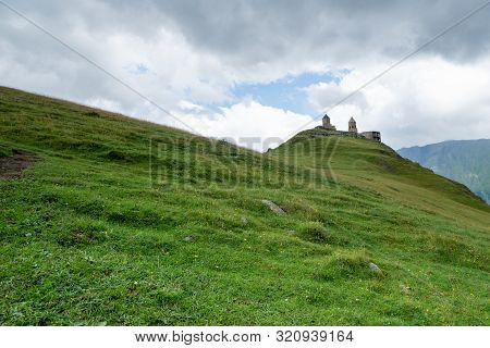 Gergeti Trinity Church Or Tsminda Sameba, Dramatic Landscaoe With Clouds. Gergeti Church Stands Near