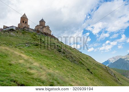 Gergeti Trinity Church Or Tsminda Sameba, Dramatic Landscaoe With Clouds. Gergeti Church Stands Near