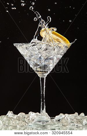 Glass Of Water, Lemon And Watersplashes On A Black Studio Background