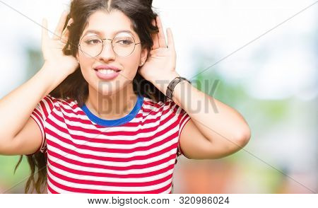 Young beautiful woman wearing glasses Trying to hear both hands on ear gesture, curious for gossip. Hearing problem, deaf