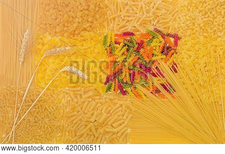 Background Of Uncooked Pasta Different Varieties, Shapes And Colors Laid Out In A Layer On A Light S