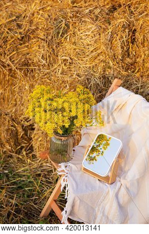 Picnic In The Field Near Straw Bales. The Setting Sun. Rustic Style - Wood Chair, Plaid, Bouquet Of 