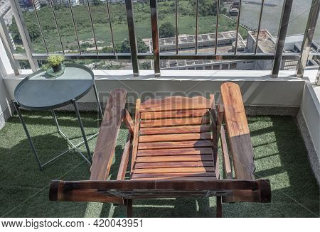 A Wooden Reclining Chair With Small Tree On Side Table With Stainless Steel Balcony Railing Overlook