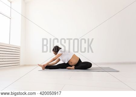 Young Flexible Pregnant Woman Doing Gymnastics On Rug On The Floor On White Background. The Concept 