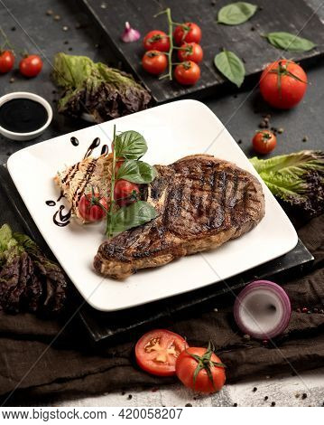 Delicious Grilled T-bone Meat On White Served Plate At Black Wooden Table. Lunch In Restaurant. Vert