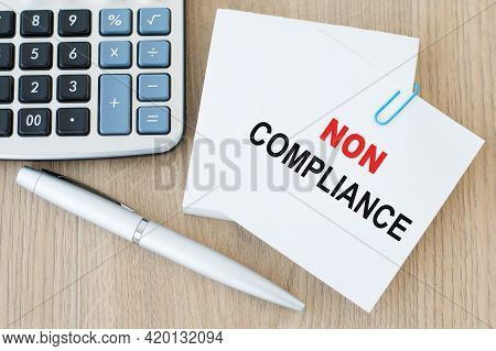 Non Compliance Text Written In White Note Paper Next To A Pen And Calculator On A Wooden Table. Busi