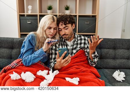 Young ill couple having medical teleconsultation using smartphone at home.