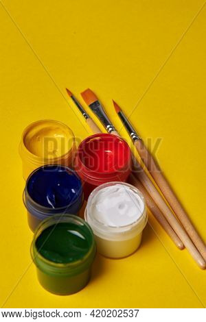 Brushes And Colored Cans Of Paint On A Yellow Background