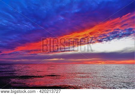 Bright Blazing Sunset Over The Black Sea. The Dark Blue Clouds Are Highlighted In Scarlet And Orange