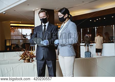 Two Receptionists Looking At The List Of Guests In Their Gadget