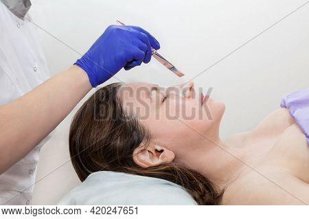 Application Of Cosmetic Mask On The Face Of A Young Woman At Spa Salon. Cosmetologist Hand In Blue P