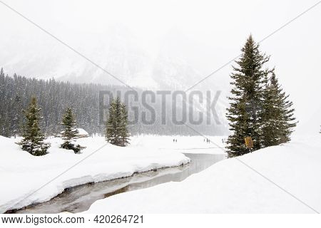 Beautiful Winter Landscape At Lake Luise, With Frozen Lake, Snowed Forest And People In The Distance
