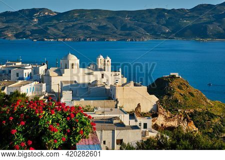 Picturesque scenic view of Greek town Plaka on Milos island over red geranium flowers and Orthodox greek church. Plaka village, Milos island, Greece