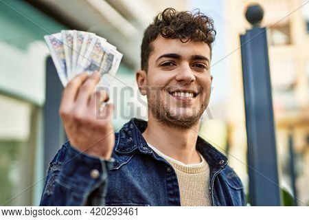 Young hispanic man smiling happy holding peruvian sol banknotes at the city
