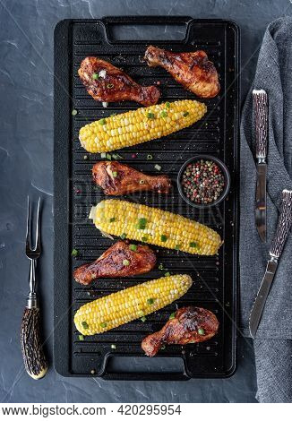 Top Down Vertical View Of A Cast Iron Grill Pan Of Bbq Chicken Drumsticks And Corn On The Cob.