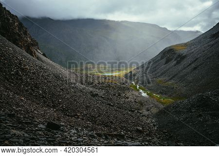 Dark Atmospheric View From Couloir With Creek To Green Mountain Valley With Lake In Overcast Weather