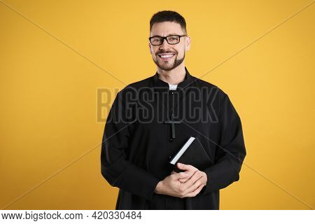 Priest In Cassock With Bible On Yellow Background