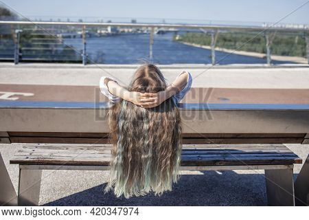 Brunette Preteen Girl With Blue Color Highlights Sitting On The Bench On The Bridge And Looking At R