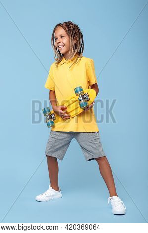 Cool Little Boy With African Dreads Play On Skateboard Like On Guitar Over Blue Background. Rock Mus