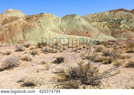 Creosote Bush And Sagebrush On A Sand Plateau With Barren Hills Beyond Embedded With Sandstone And S