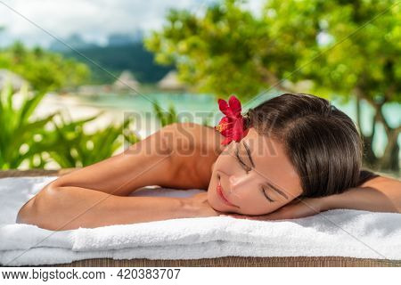 Body care massage at outside spa on beach at luxury vacation resort. Asian beauty woman relaxing sleeping lying on table during aromatherapy treatment with coconut oil.