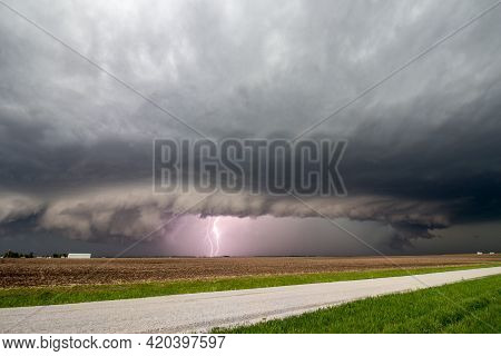 Lightning Strikes As A Supercell Thunderstorm Approaches A Rural Road. A Shelf Cloud Marks The Edge 