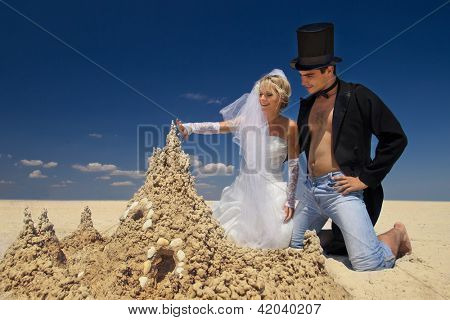 En ung och vacker nyligen gift par njuter på stranden nära sand slott vid havet kanten