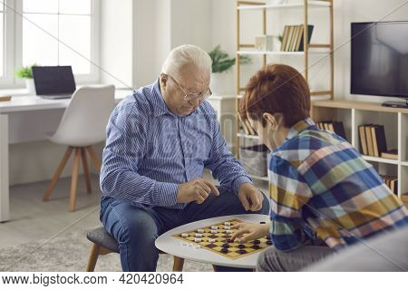 Senior Concentraited Man Grandfather Sitting And Playing Checkers With His Grandson