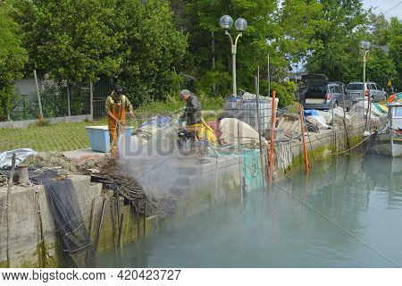 Punta Sdobba, Italy - June 14th 2020. Fishermen Untangle And Clean Their Nets With A Water Jet In Th