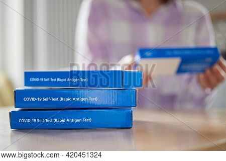 Close Up Of Woman At Home Reading Instructions On Supply Of Covid-19 Rapid Antigen Self-testing Kits