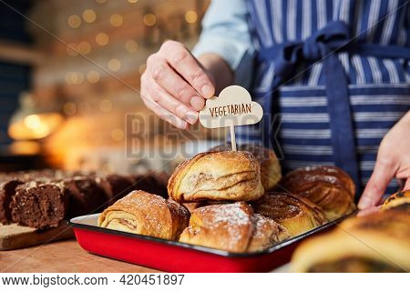 Sales Assistant In Bakery Putting Vegetarian Free Label Into Freshly Baked Baked Cinnamon Bun