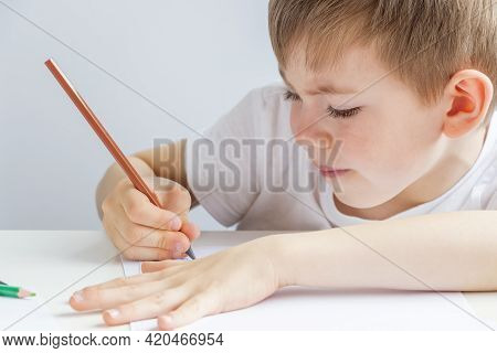 Focused Preschooler Little Boy 5-6 Years Painstakingly Draws Drawing By Pencil. Doing Homework, Draw