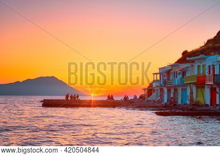 People enjoy scenic sunset in picturesque Klima village above Aegean sea on Milos island in Greece