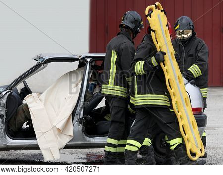 Team Of Firefighters At The Rescue To The Injured With A Yellow Stretcher After The Road Accident