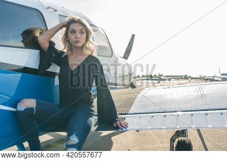 A gorgeous young blonde model poses outdoors with a single engine aircraft at a local airport