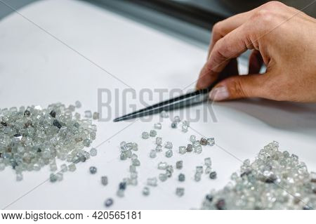 Manual Sorting Of Diamonds. A Hand With Tweezers Transfers Diamonds From One Pile To Another. Discar