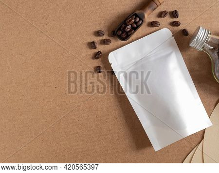 Roasted Coffee Beans In White Paper Bag With Zipper And Wooden Scoop, Glass Bottle On Brwon Backgrou