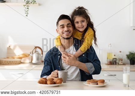 Happy Middle Estern Father And Daughter Posing In Kitchen While Eating Snacks