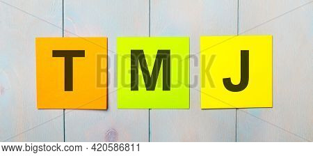 Three Colored Stickers With The Text Ada Americans With Tmj On A Light Blue Wooden Background