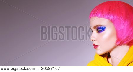 High fashion model with bright glitter make-up and pink hair poses at studio in trendy yellow clothes. Make-up and hairstyle. Sport chic clothing. Party style.