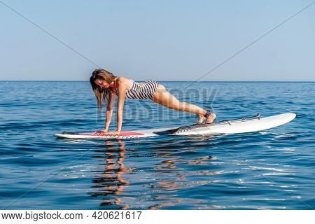 Sporty Girl On A Glanders Surfboard In The Sea On A Sunny Summer Day. In A Striped Swimsuit, It Is I