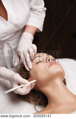Spa And Beauty Clinic. Cosmetologist Doctor Making Marks On Client Face With Medical Marker, Skin Pr