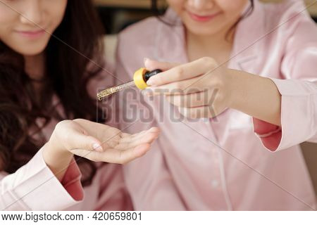 Young Woman With Pipette Dropping Hydrating Serum On Hand Of Her Friend