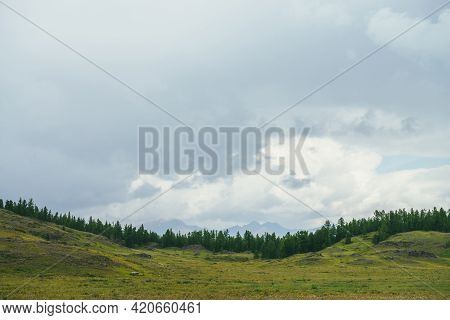 Beautiful Green Scenery With Forest Edge On Hills Against Mountains Silhouettes On Horizon Under Clo