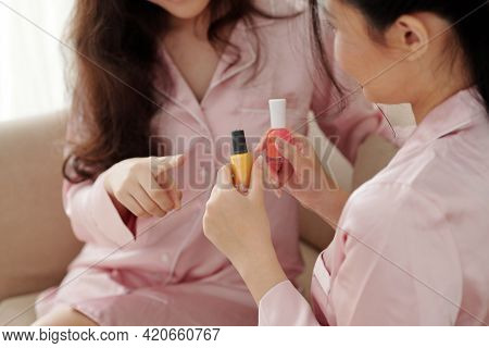 Hands Of Young Woman Showing Bottles With Hot Pink And Bright Yellow Nail Polishes To Friend