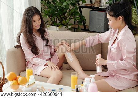 Young Woman Applying Rich Moisturizing Lotion On Leg Of Her Friend