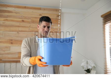 Emotional Man Collecting Water Leaking From Ceiling Indoors. Damaged Roof